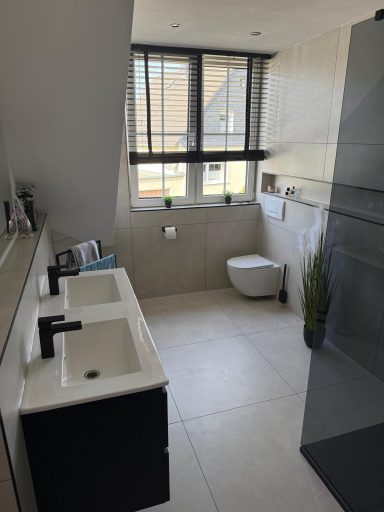 Moderne Badezimmeransicht mit Doppelwaschbecken, Toilette und Fenster.